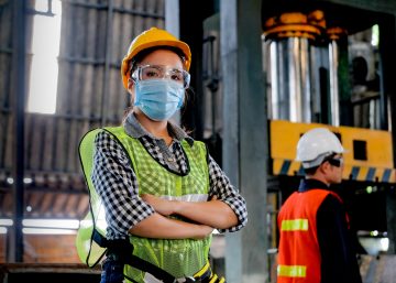 Factory woman worker or technician with hygienic mask stand with confident action with her co-worker as background